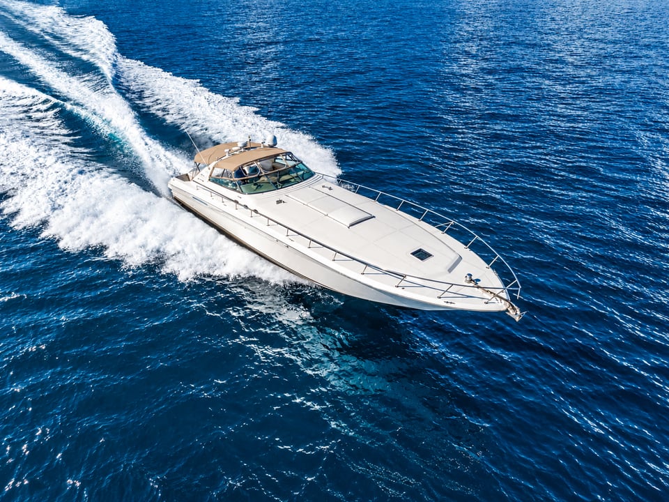 Aerial view of a white motor yacht cruising through deep blue water with a sweeping white wake