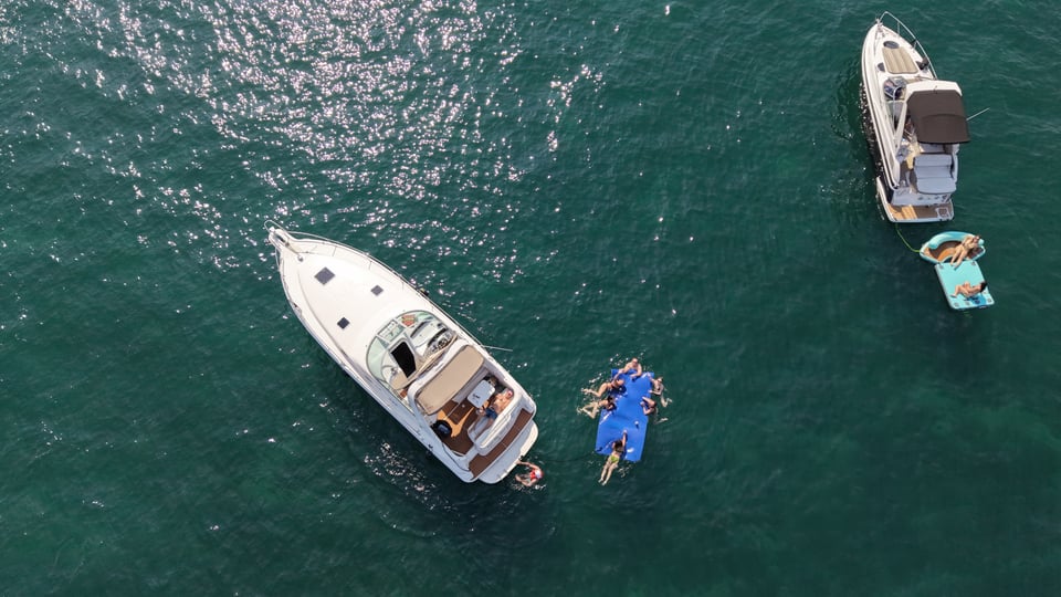 Aerial view of two yachts at anchor with guests swimming and relaxing on floating mats